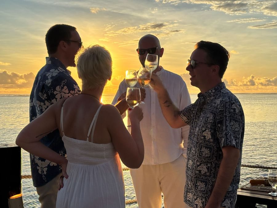 Four people toasting with wine glasses at sunset overlooking the ocean at Warwick Fiji Resort and Spa.