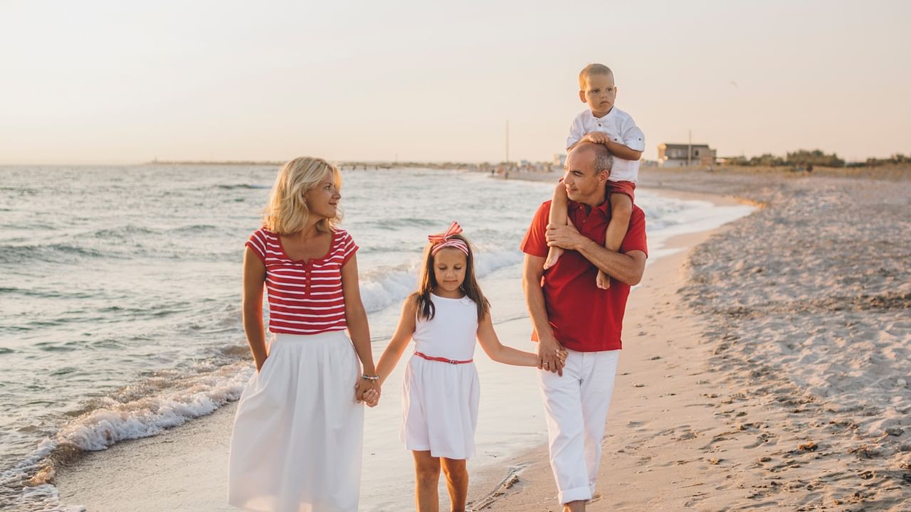 Family of four walking hand in hand along a sandy beach at sunset with calm ocean waves