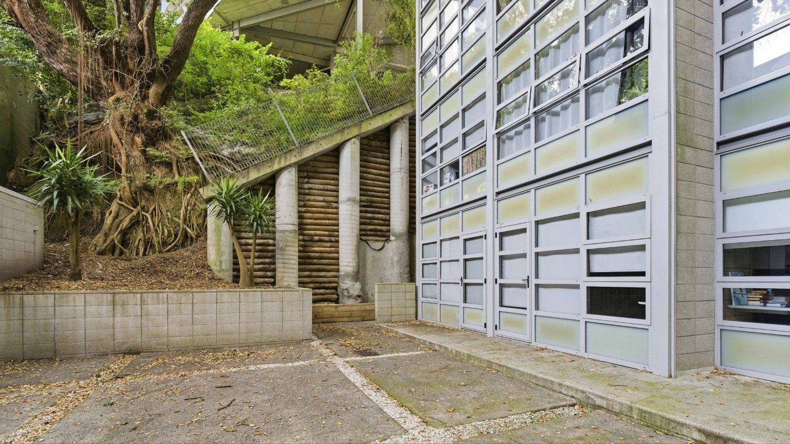 Exterior of a modern building with large glass windows and surrounding greenery at Student Living Auckland Beach.