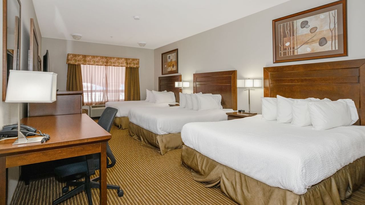 Hotel room with three queen beds, work desk, TV, and a large window