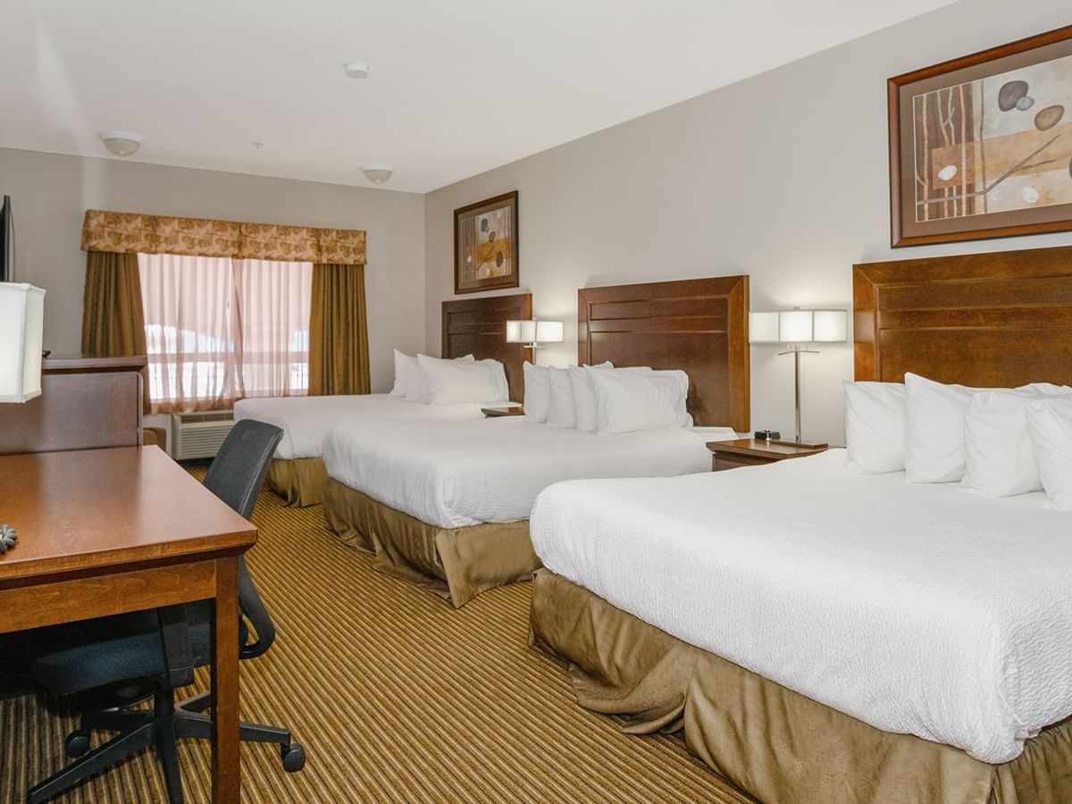 Hotel room with three queen beds, work desk, TV, and a large window