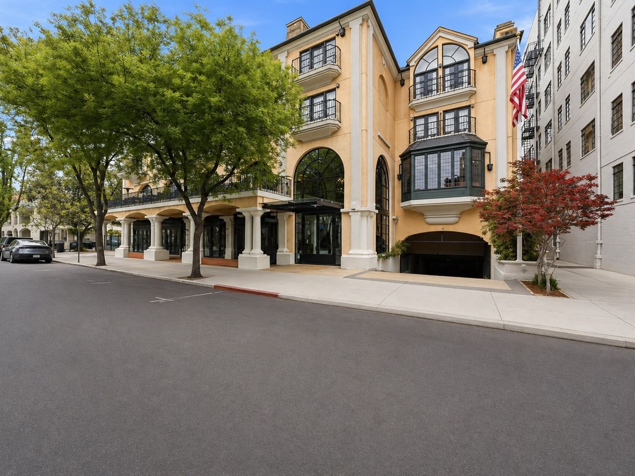 Street view of a Mediterranean-style hotel building with arched entrance and tree-lined sidewalk at el PRADO Hotel