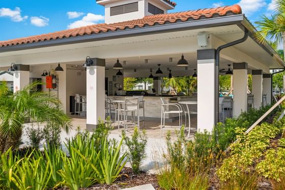 Outdoor bar at Vista Cay Resort with covered seating area, surrounded by lush greenery under a blue sky with white clouds.