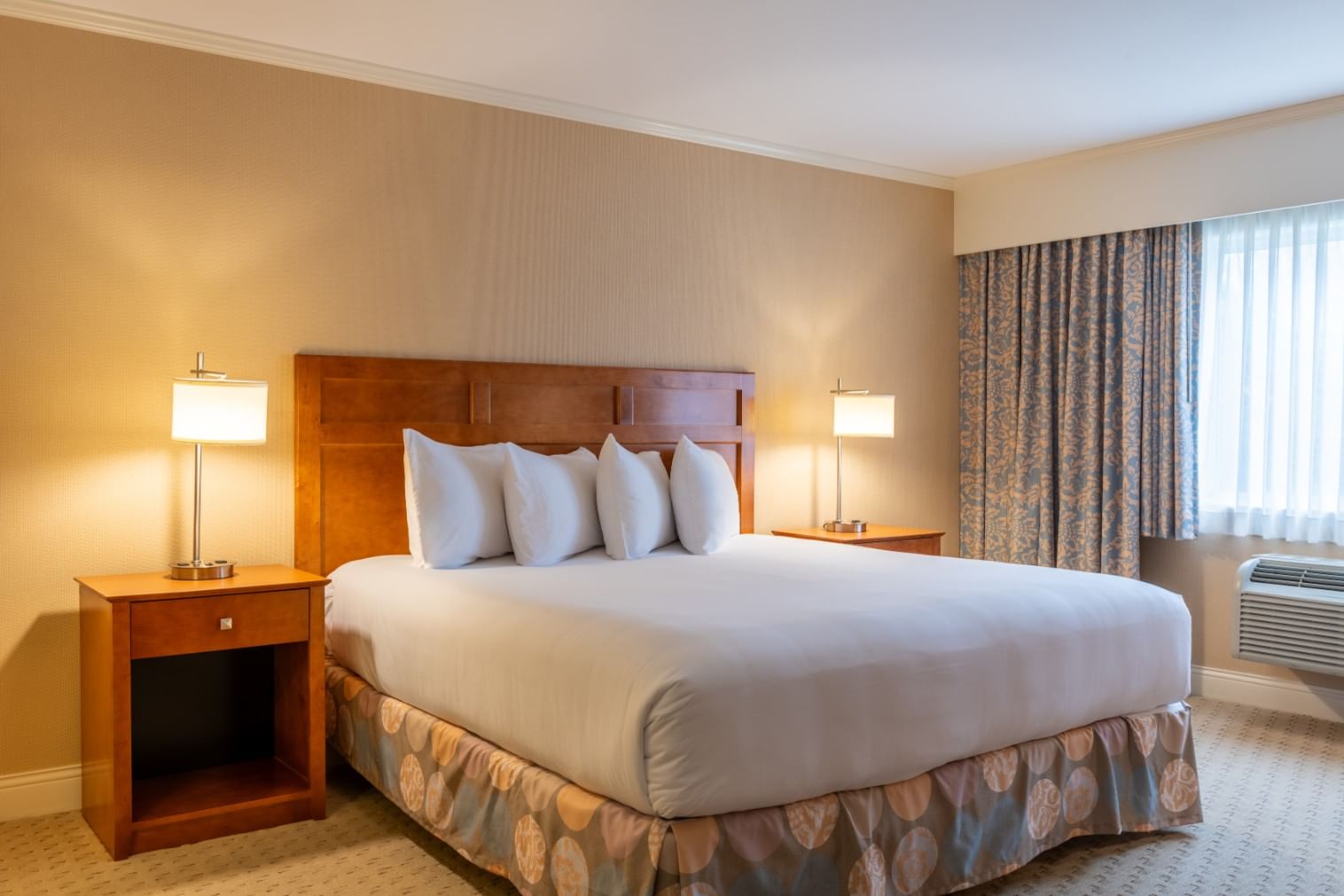 A hotel room with a king-sized bed, two nightstands with lamps, and a window with a view.
