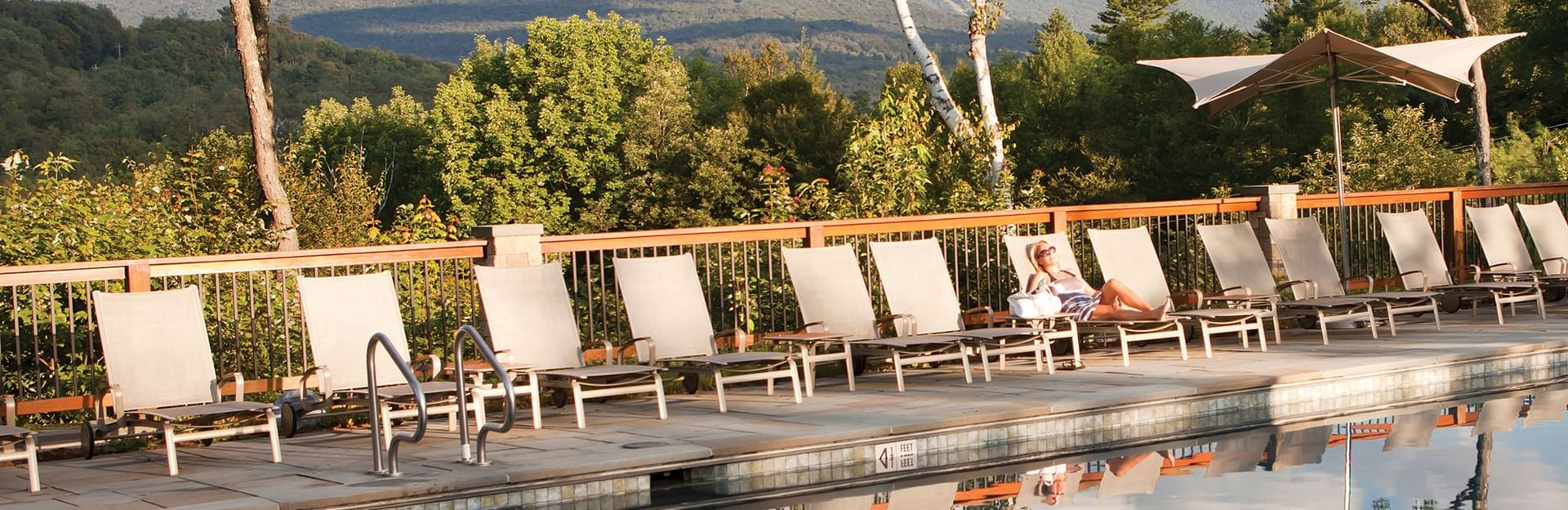 Guest relaxing on a lounge chair by the pool deck, framed by birch trees and mountain views at Topnotch Stowe Resort