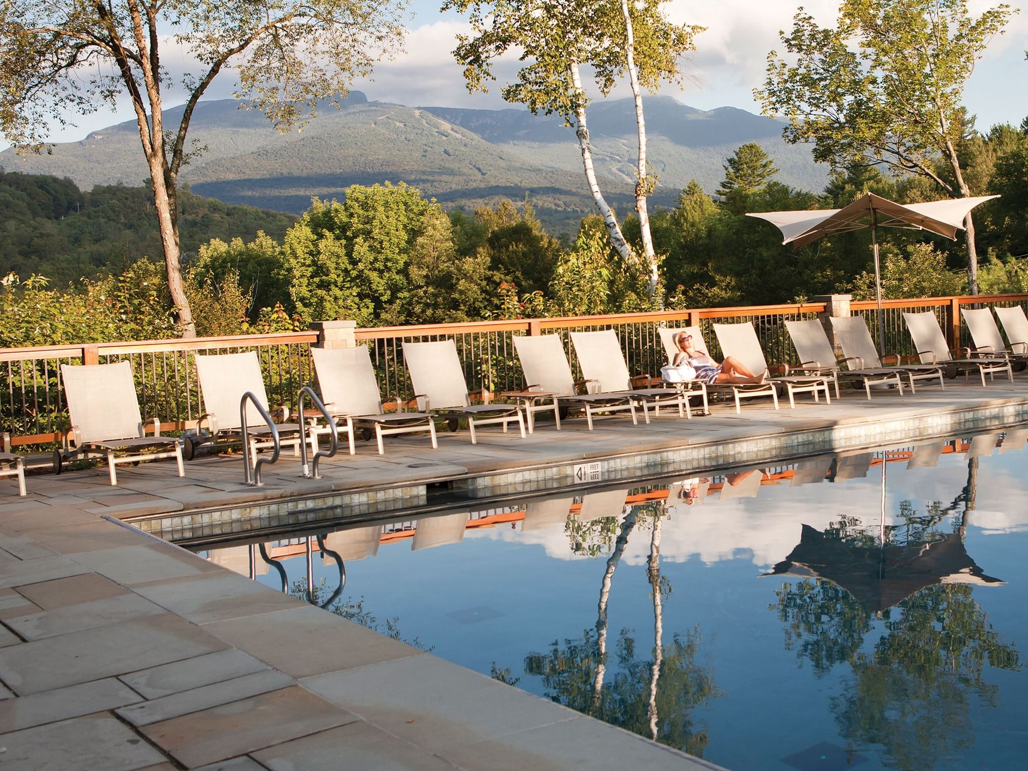 Outdoor pool with lounge chairs overlooking mountain views and lush greenery under a partly cloudy sky.