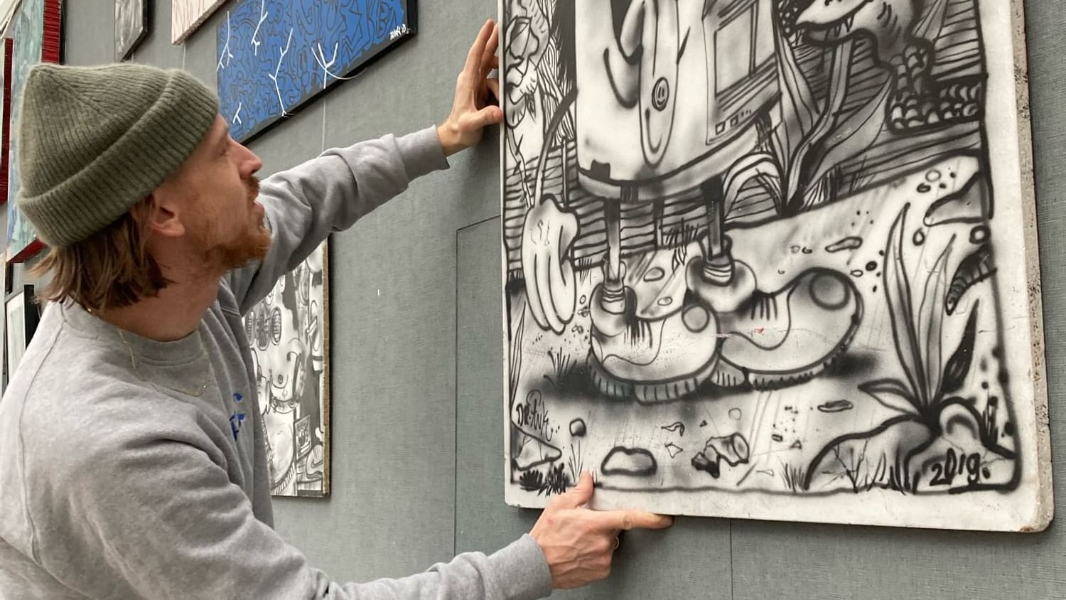 The artist hanging up his art on a wall.