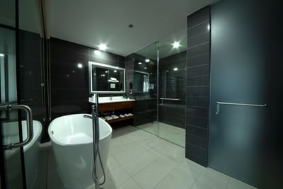 Modern bathroom with freestanding tub, wooden storage, double sink, & glass shower enclosure at D Sabana Hotel
