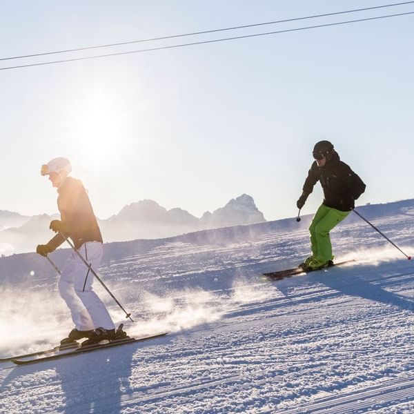 Two people skiing down a hill near Falkensteiner Hotels