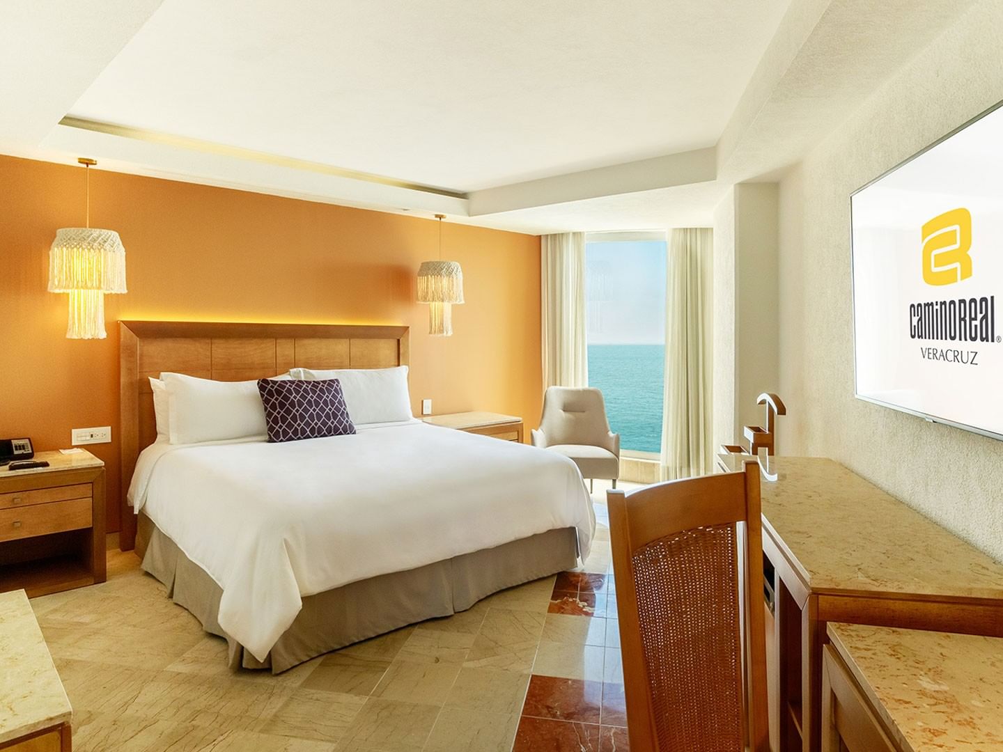 King Deluxe room with a large bed, wooden furniture, a wall-mounted TV, and an ocean view at Camino Real Veracruz