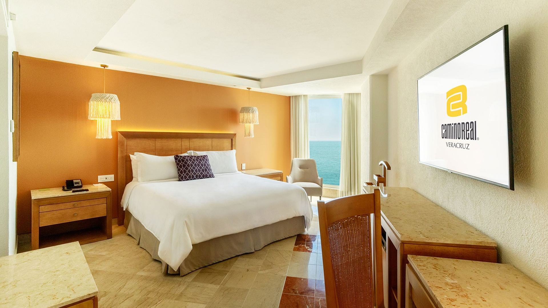 King Deluxe room with a large bed, wooden furniture, a wall-mounted TV, and an ocean view at Camino Real Veracruz