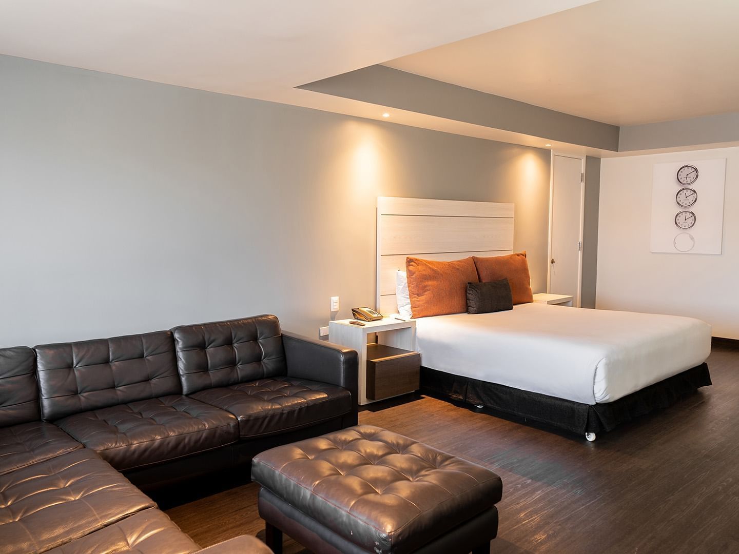 King Junior Suite featuring a black leather sectional sofa and ottoman facing a white cozy bed at Real Inn Tijuana