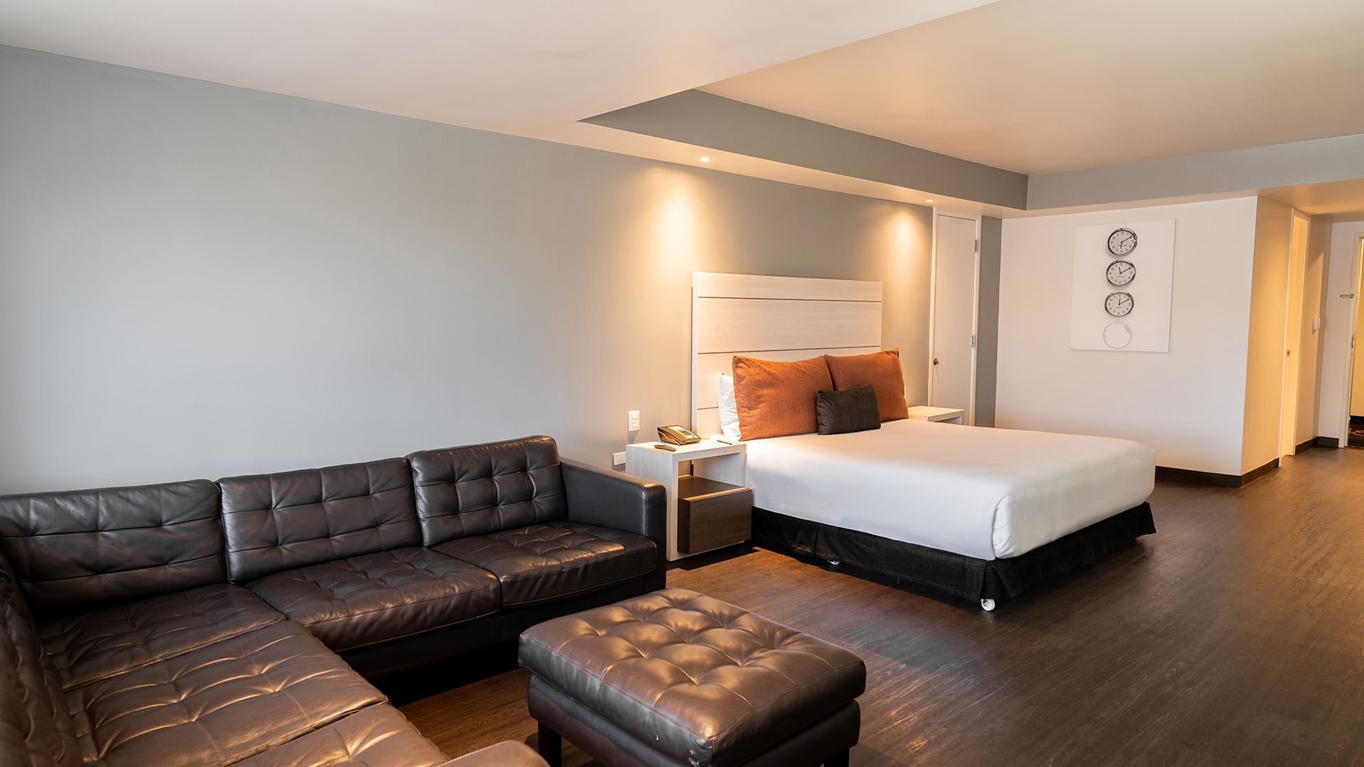 King Junior Suite featuring a black leather sectional sofa and ottoman facing a white cozy bed at Real Inn Tijuana