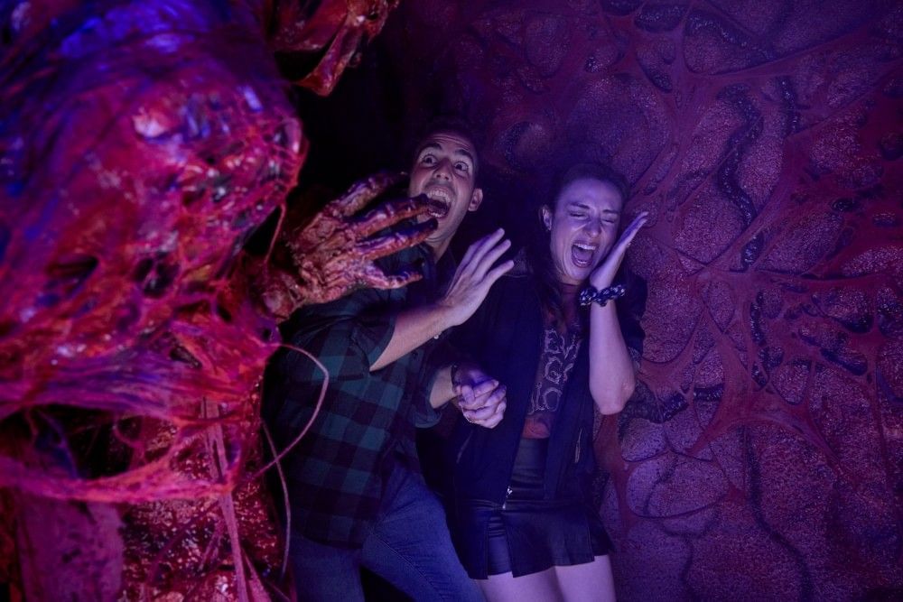 A man and woman holding hands scream in fright as a gory figure jumps out of the shadows at Halloween Horror Nights 35 in Orlando.