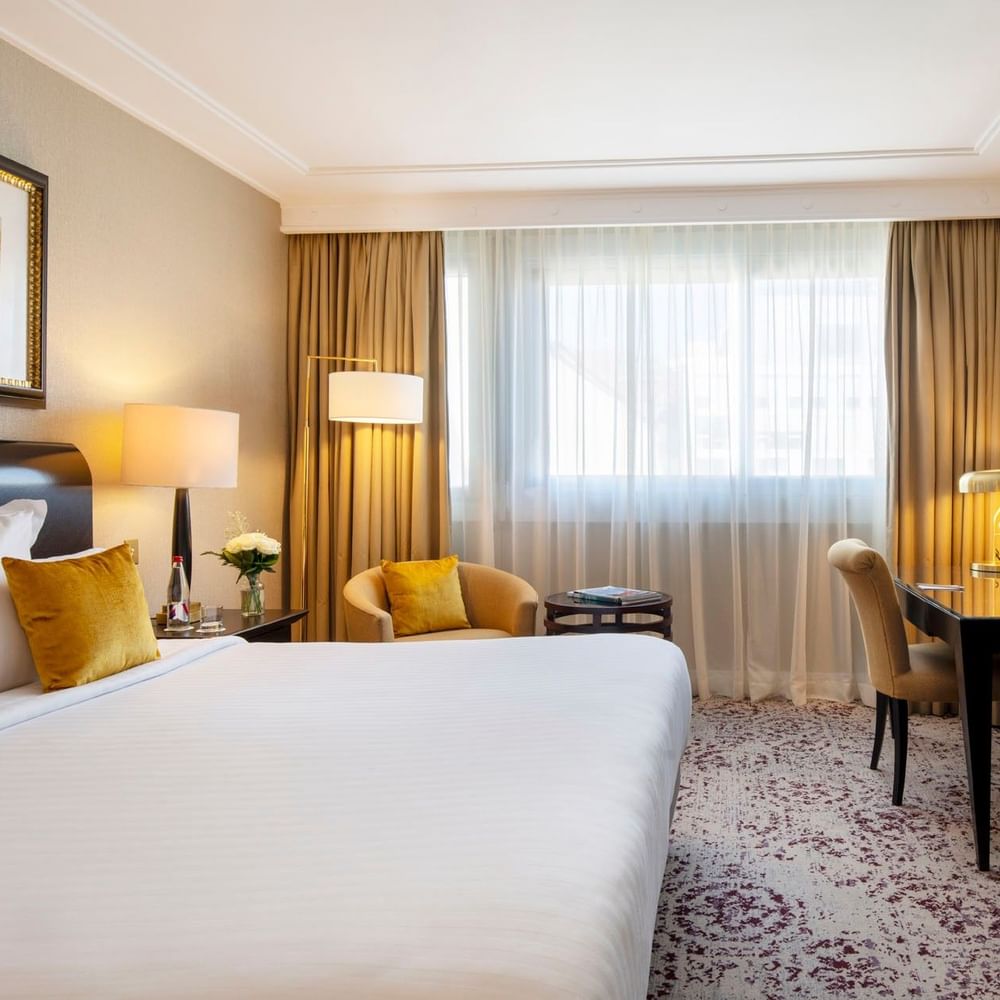 Chambre élégante avec un lit king-size, un coin salon et une grande fenêtre au Warwick Champs-Élysées Paris.