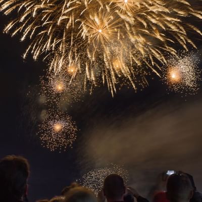 Menschen beobachten ein Feuerwerk mit goldenen und leuchtenden Effekten in der Nacht.