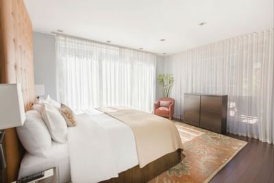 Garden Terrace bedroom with large bed, white curtains, wooden cabinet, and a rug with a chair near the window.
