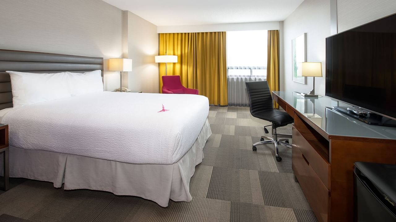 Hotel room with a large bed, desk, TV, and yellow curtains on the window.