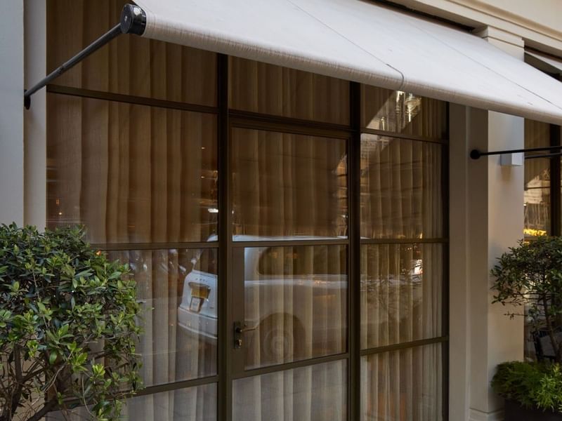 May Fair Kitchen restaurant entrance with white awning, glass doors, and green plants in planters.
