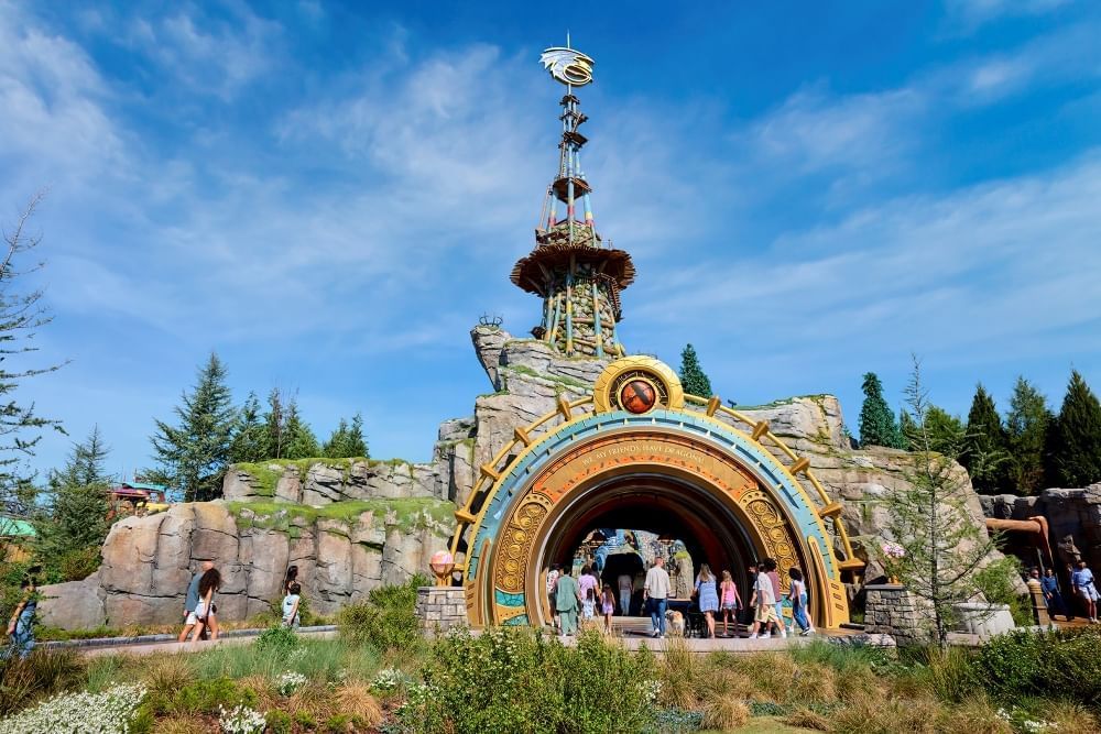 A large futuristic-looking arch at the front of a rock wall with a tall tower and a dragon emblem sitting on top.
