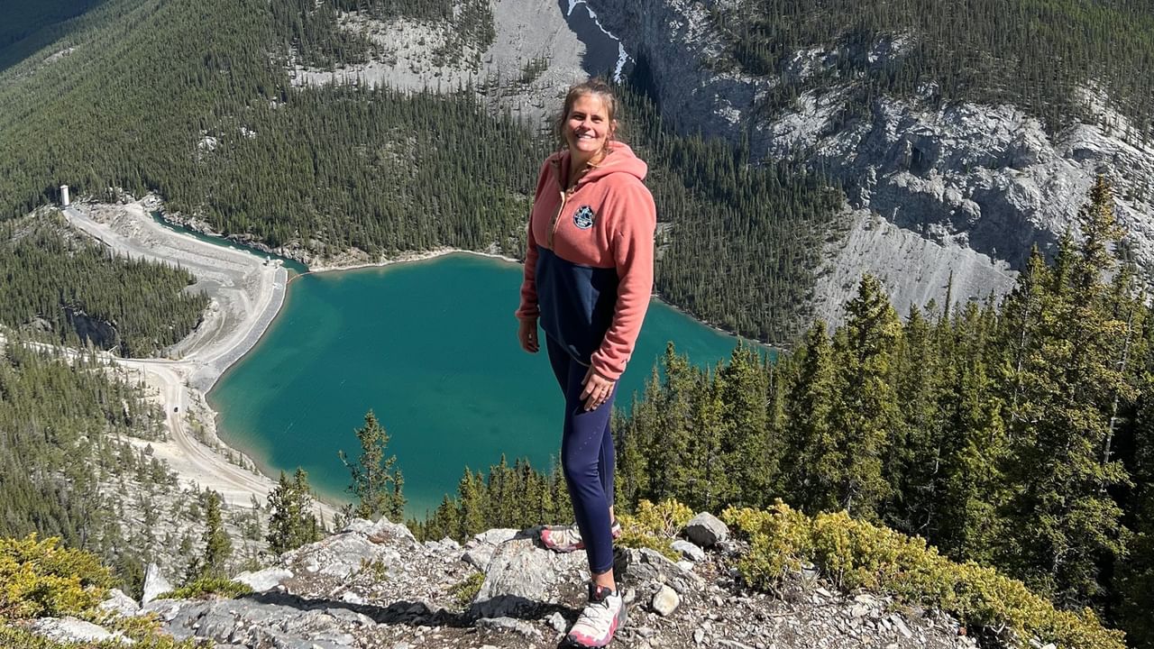 A person poses at the top of a mountain during a hike in Canmore on a sunny day.