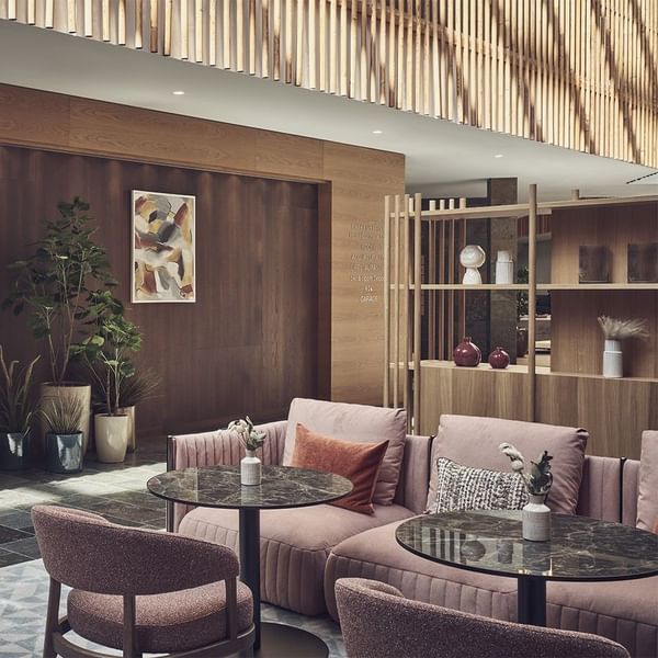 Moderne Lounge mit rosa Couches, Holzmöbeln, Pflanzen und abstraktem Gemälde an der Wand.