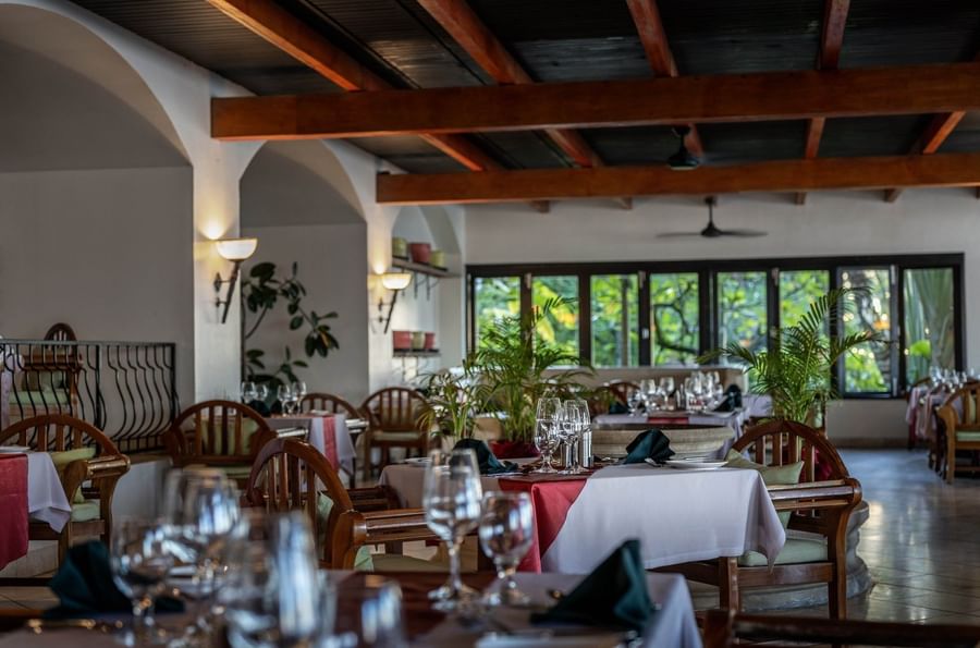Dining tables with red linens by wooden chairs under a beamed ceiling in Pappagallo at Warwick Fiji Resort and Spa
