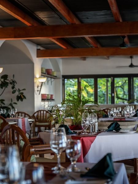 Dining tables with red linens by wooden chairs under a beamed ceiling in Pappagallo at Warwick Fiji Resort and Spa