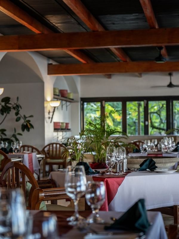 Dining tables with red linens by wooden chairs under a beamed ceiling in Pappagallo at Warwick Fiji Resort and Spa