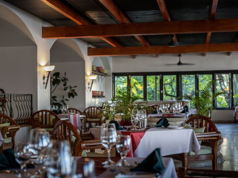 Dining tables with red linens by wooden chairs under a beamed ceiling in Pappagallo at Warwick Fiji Resort and Spa