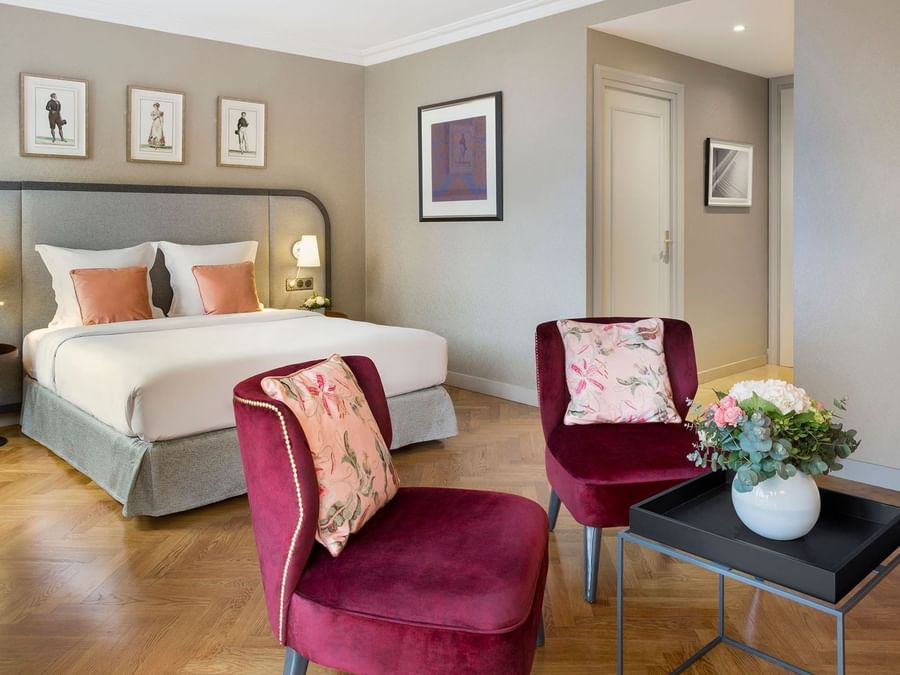Seating area by the cozy bed with a cushioned headboard and wooden floors in the Deluxe Room at Warwick Reine Astrid - Lyon