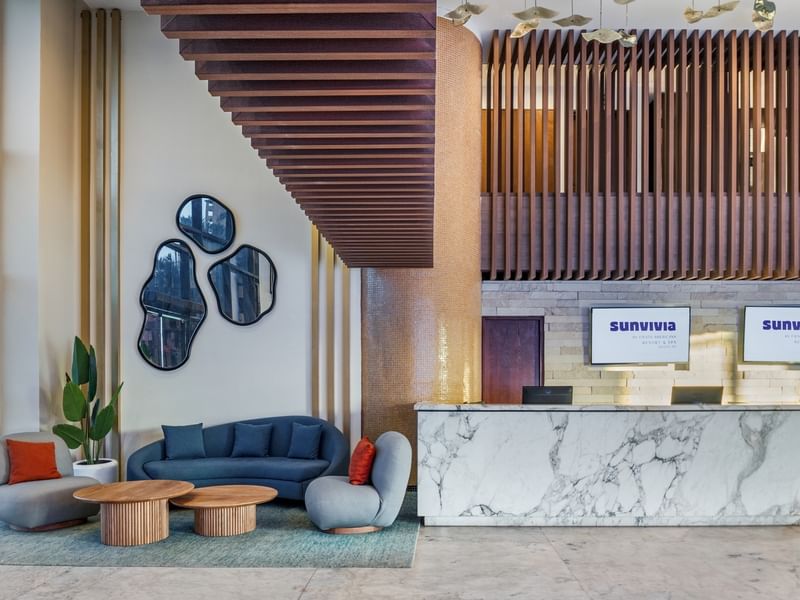 Elegant lobby at Sunvivia Mazatlán featuring a marble front desk, stylish blue seating, and modern decor