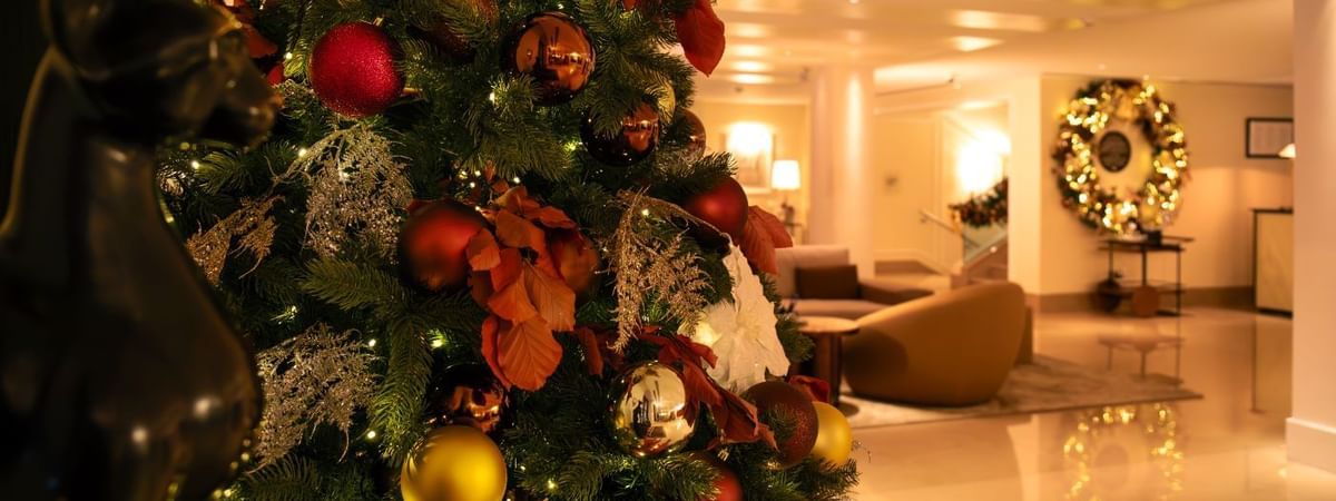 Decorated Christmas tree with colorful ornaments and lights at The May Fair Hotel lobby with festive wreath in background