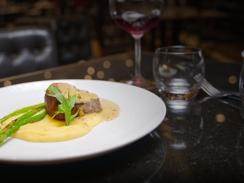 A gourmet plated steak with creamy mashed potatoes and asparagus, served with a glass of red wine at Camino Real