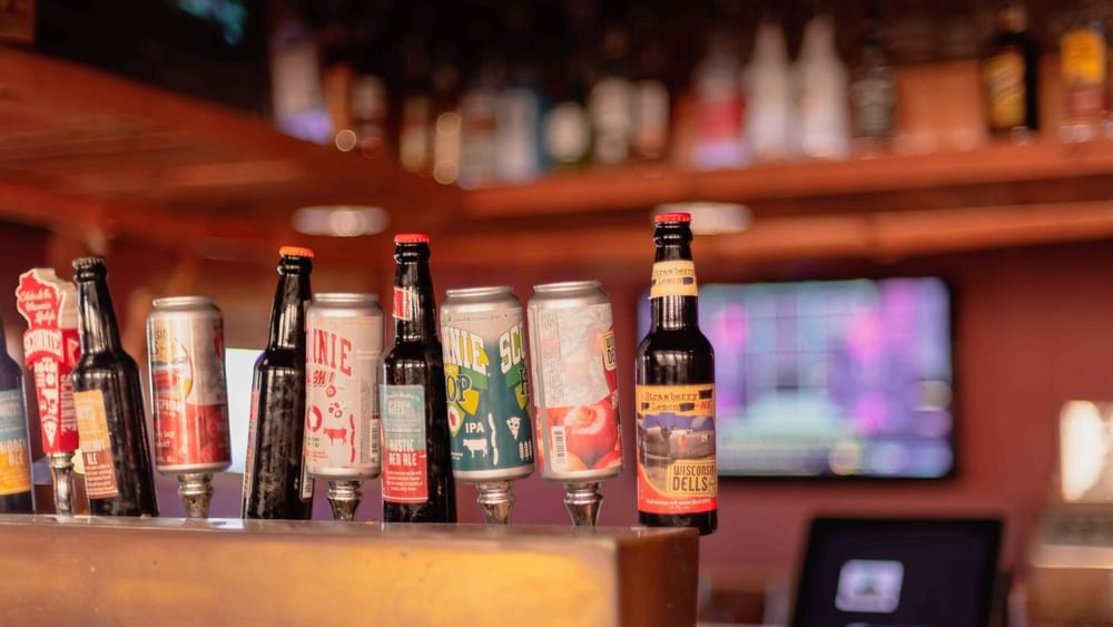 Beer bottles and cans on a wooden bar counter by a blurry screen at Warwick Denver