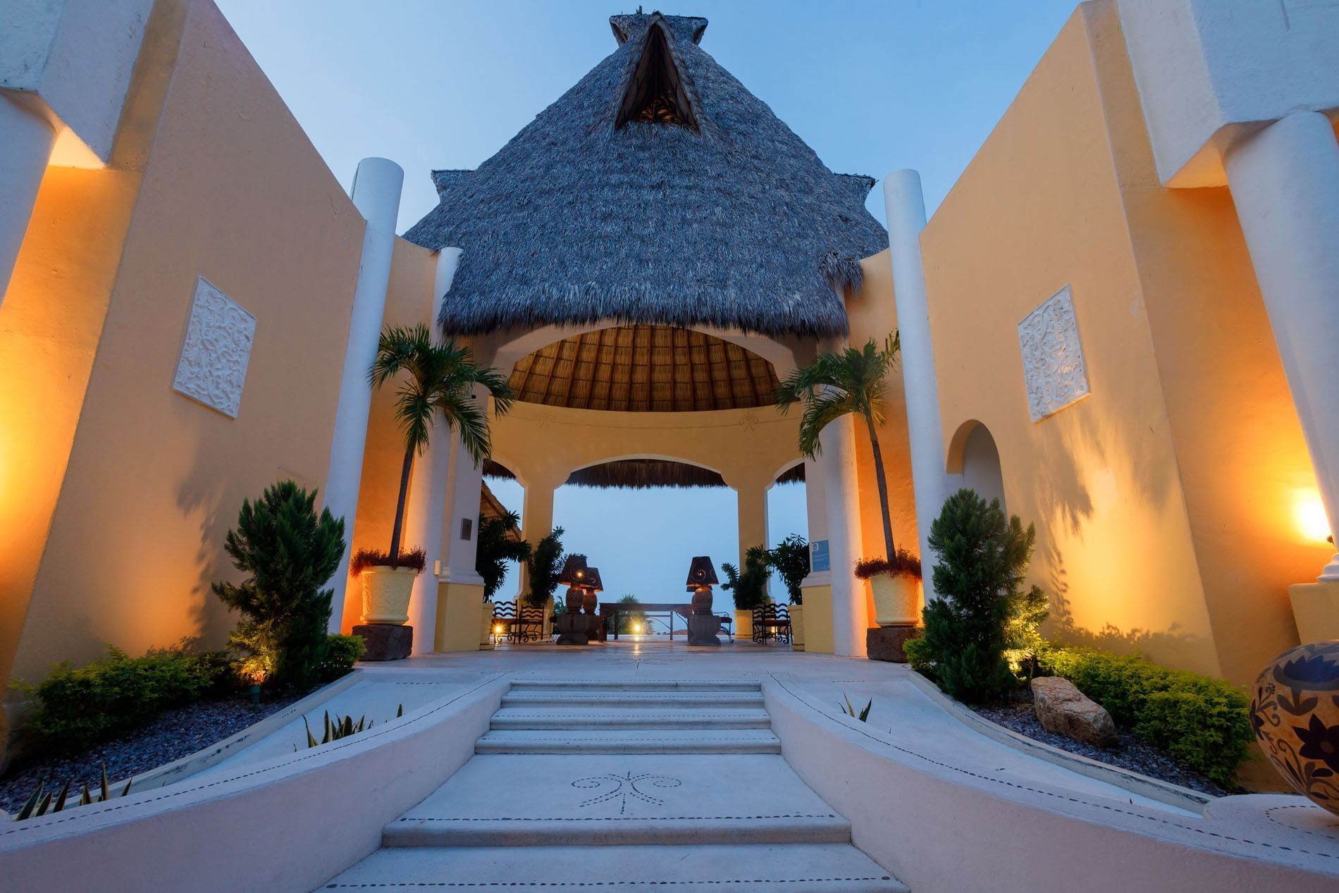 Grand entrance featuring a high thatched palapa roof and symmetrical stone architecture at Quinta Real Acapulco