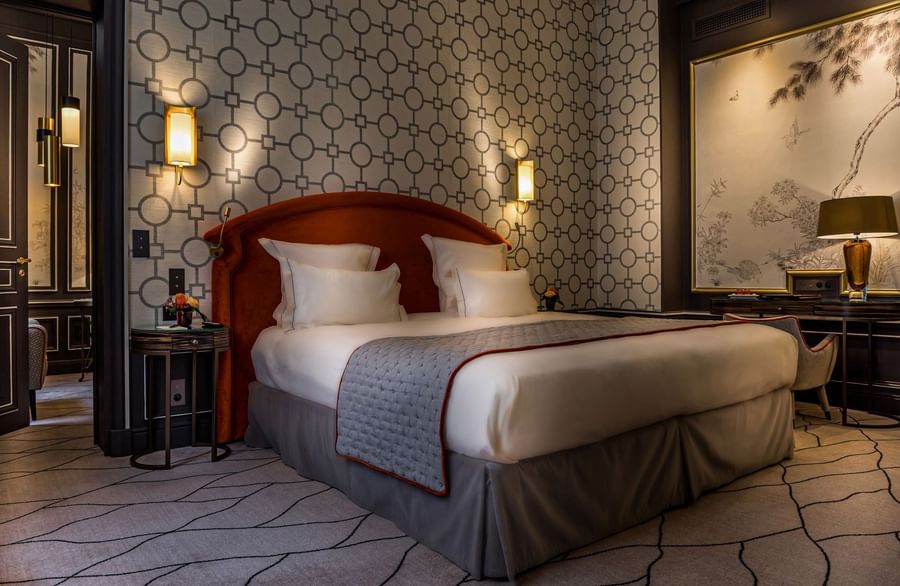 Bed with a side table set against a patterned wall in the Deluxe Suite Parisienne at Hotel Westminster Paris