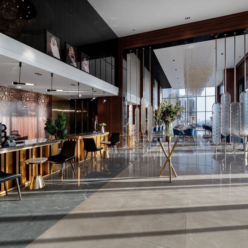 Modern hotel lobby with wooden reception desk, black chairs, glass wall, and decorative elements.