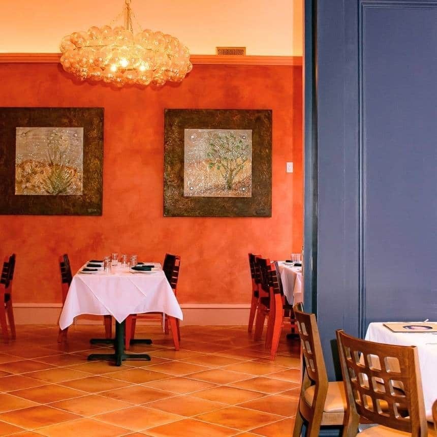A dining area with tables set for meals, a chandelier, and artwork on the walls.