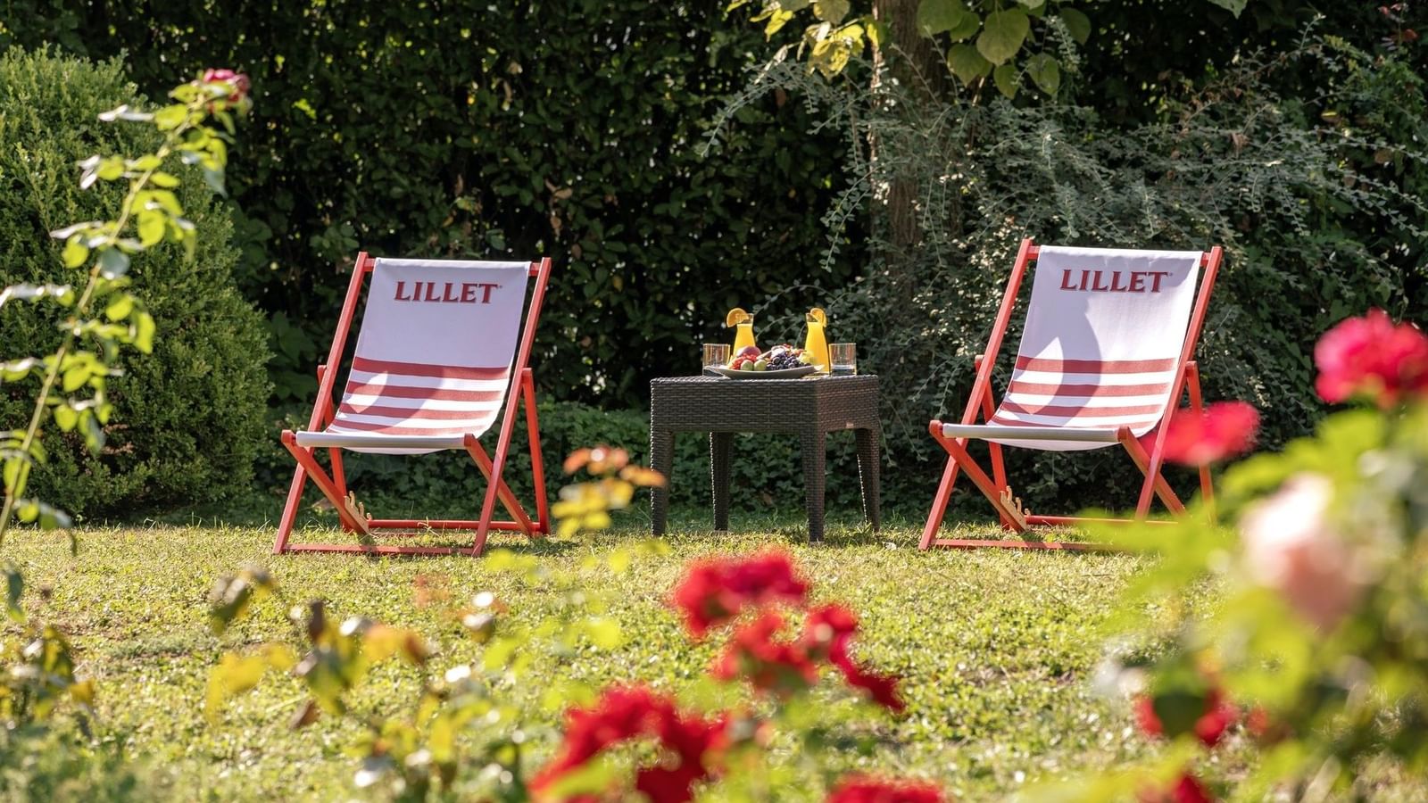 Two Lillet-branded deck chairs and a small black table with drinks in a lush garden at Warwick Reine Astrid - Lyon