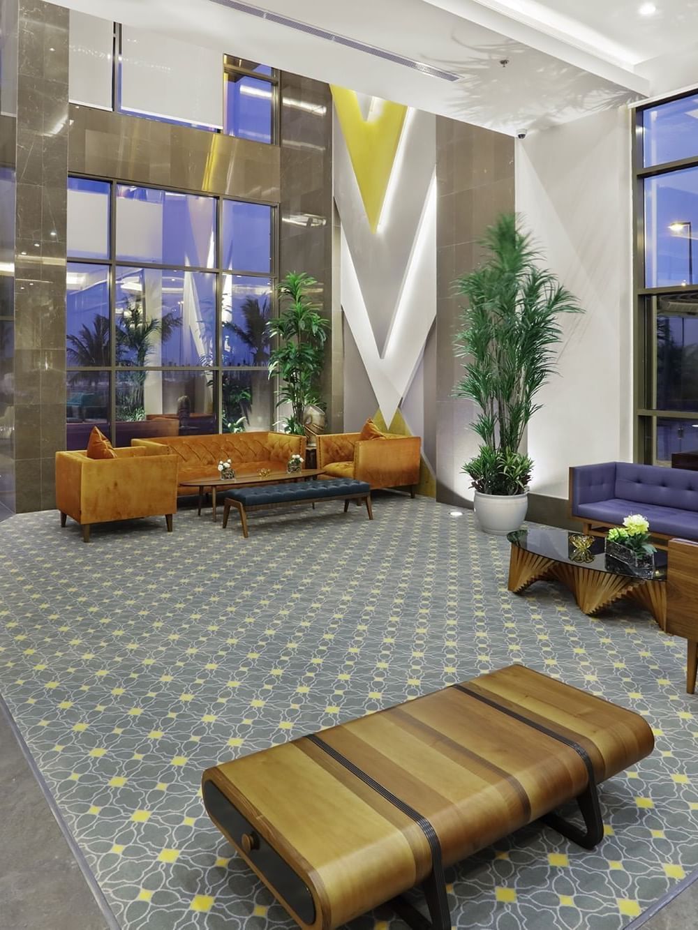 Hall d'entrée avec canapés orange et bleus près d'une grande baie vitrée, à côté d'un banc en bois, au Naviti By Warwick Dammam