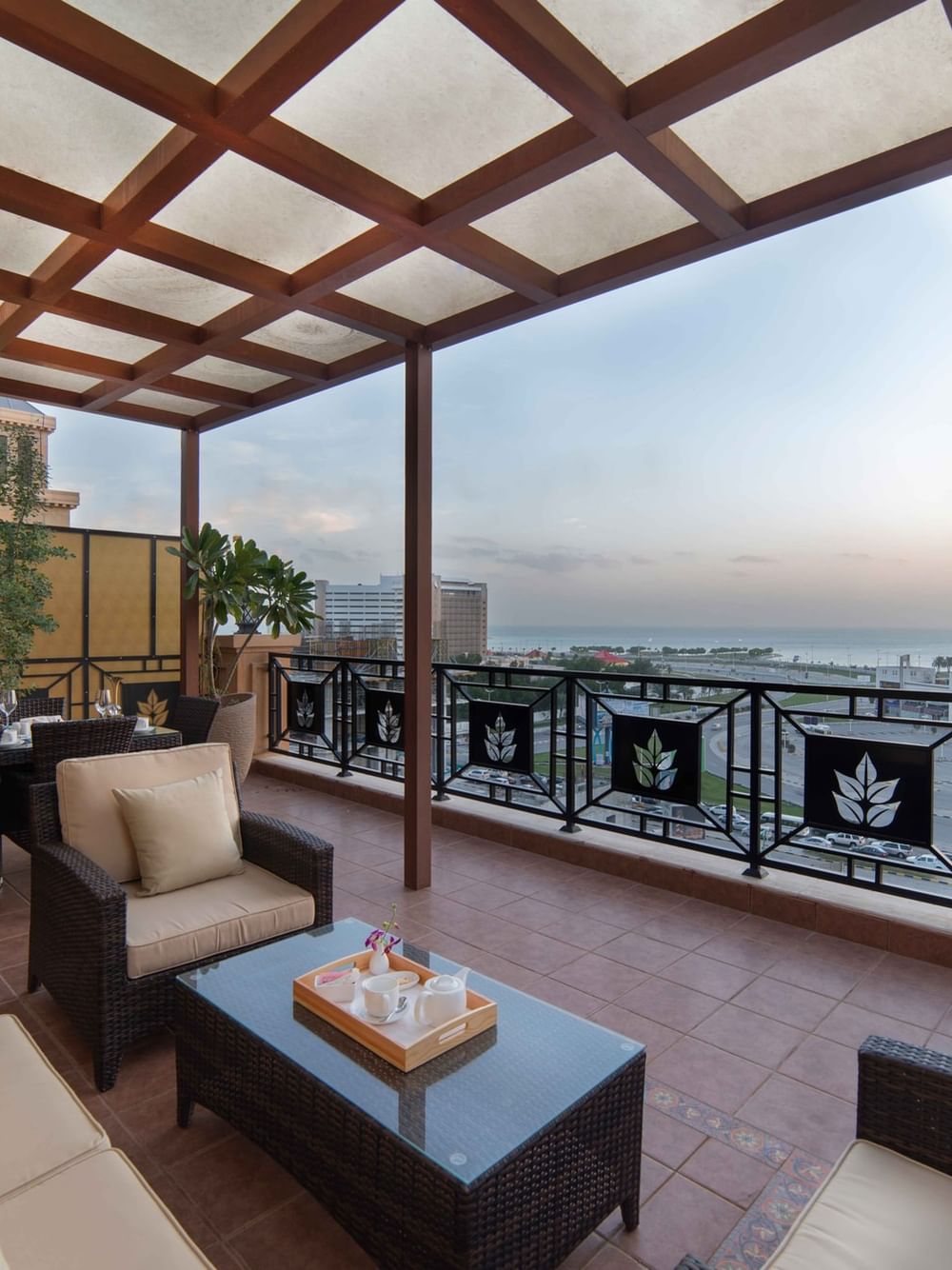 Penthouse Villa furniture on a balcony with a tea set on a table under a pergola at Warwick Al Khobar