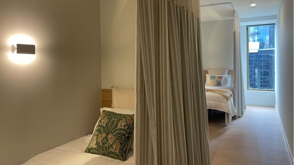 A cozy bedroom with beds, curtains, and a lamp within a 4 Bedroom Twin Share Apartment at UniLodge Brisbane City.