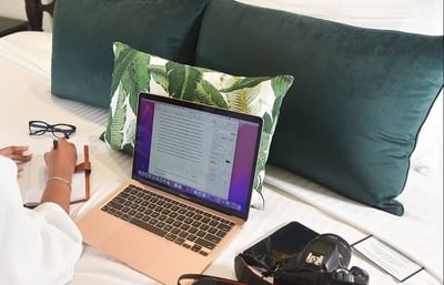 A person sitting on a bed with a laptop and a pillow in Penthouse Two Bedroom Suite at Courtleigh Hotel & Suites