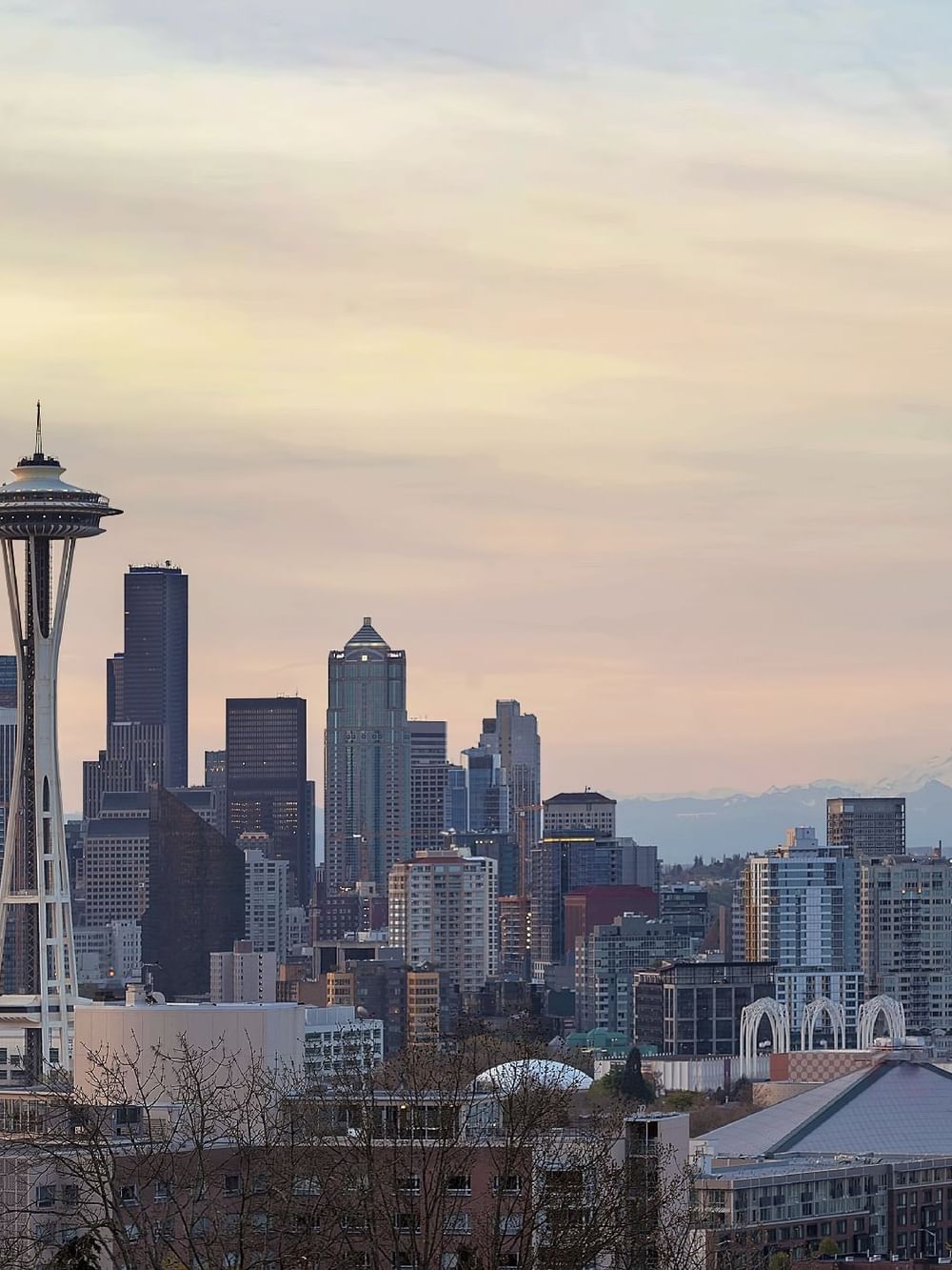 The Space Needle by high-rise buildings near snow-capped mountains at sunset near Warwick Seattle