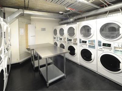 A room with multiple washing machines and a metal table at UniLodge Auckland City.
