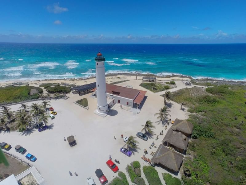 Aerial view of a white lighthouse with a red roof, surrounded by palm trees and parked cars at Fiesta Americana Travelty