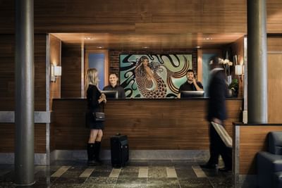 Guest with luggage standing before staff at the front desk beneath a mural painting at Harborside Inn Boston