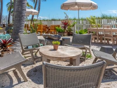 Outdoor beach seating area with wicker chairs and wooden tables at The Savoy Hotel & Beach Club