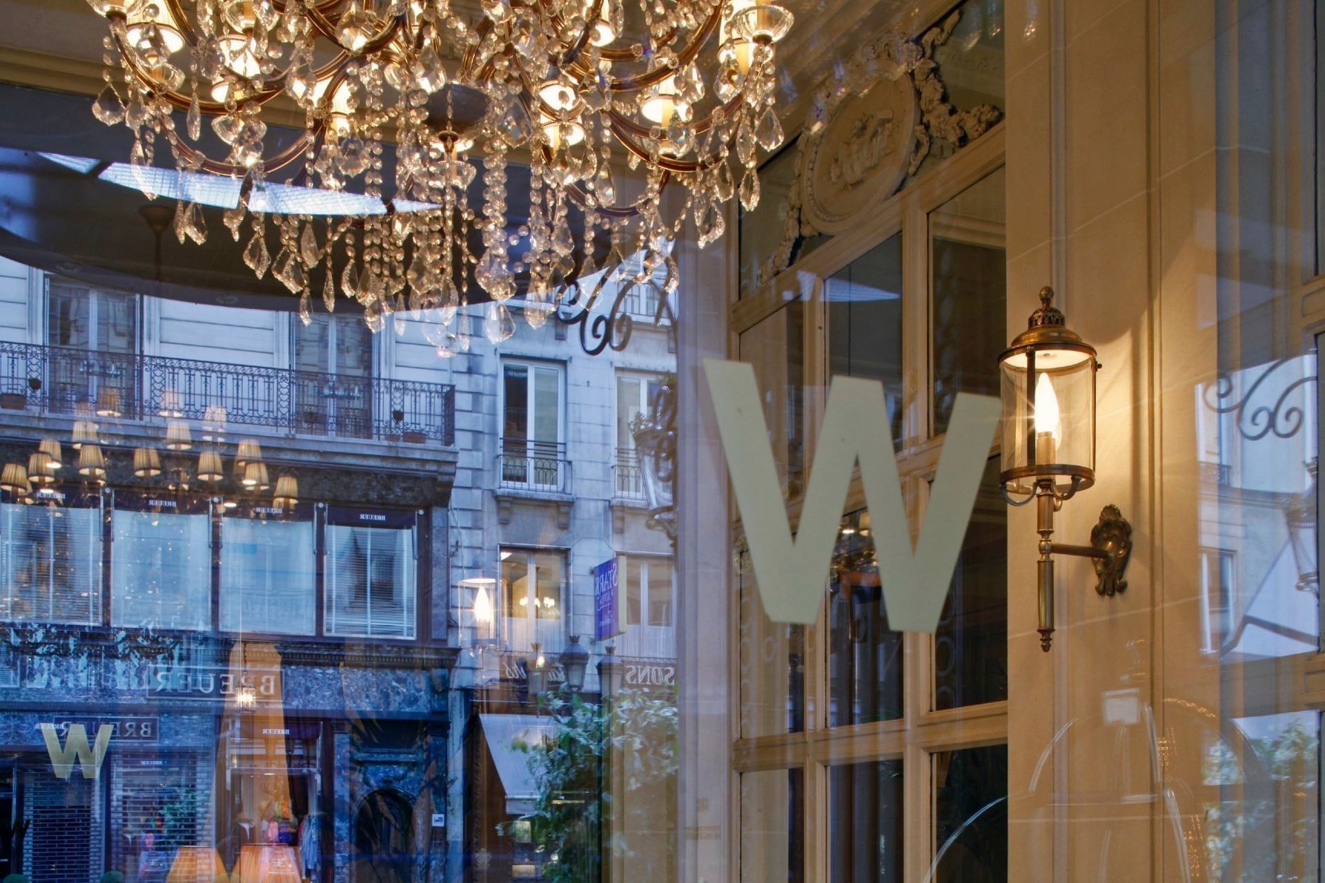 Decorative letter W etched on glass by a warm wall lamp, under a crystal chandelier at Hotel Westminster Paris